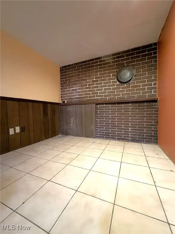 Unfurnished room featuring light tile patterned floors, wood walls, wainscoting, and brick wall