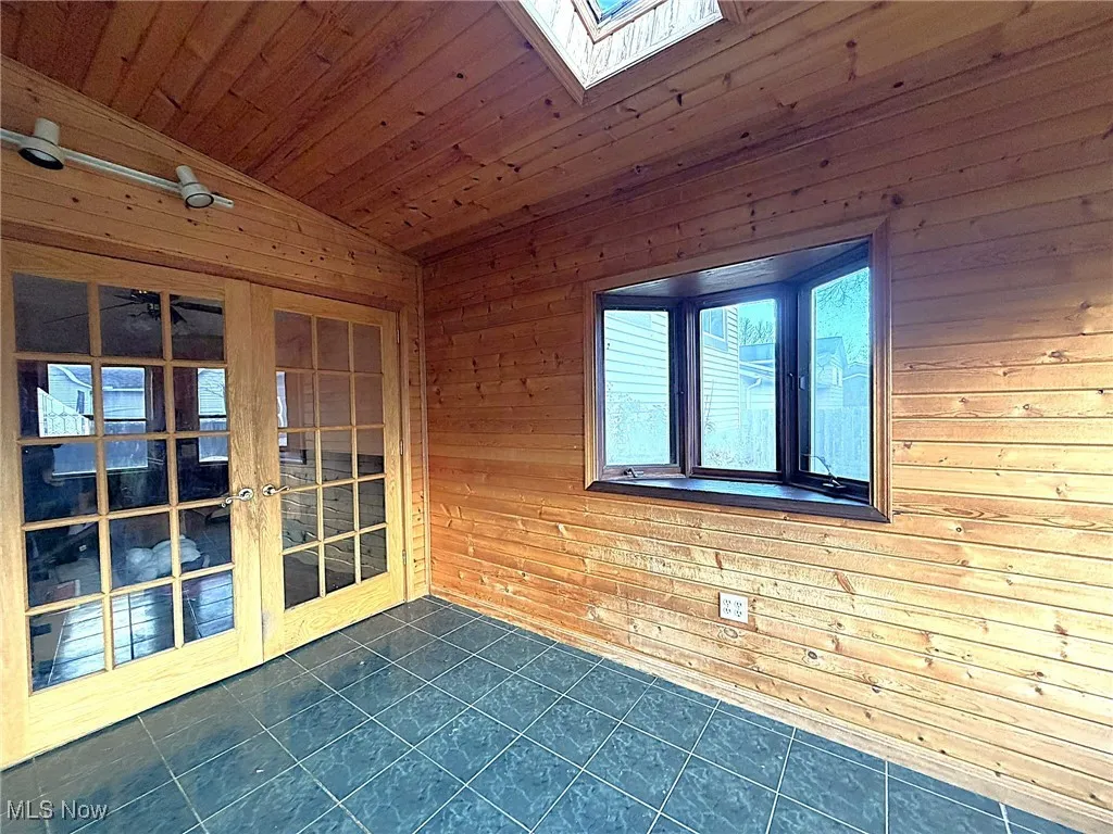 Spare room with wooden walls, vaulted ceiling, a skylight, dark tile patterned flooring, and wood ceiling