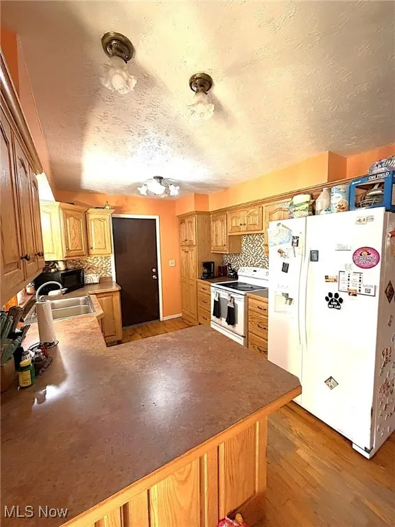 Kitchen featuring white appliances, a textured ceiling, backsplash, light wood-style floors, and a peninsula