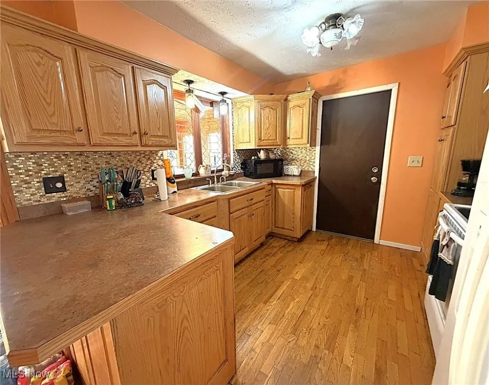 Kitchen with tasteful backsplash, a textured ceiling, light wood-style flooring, electric range, and black microwave