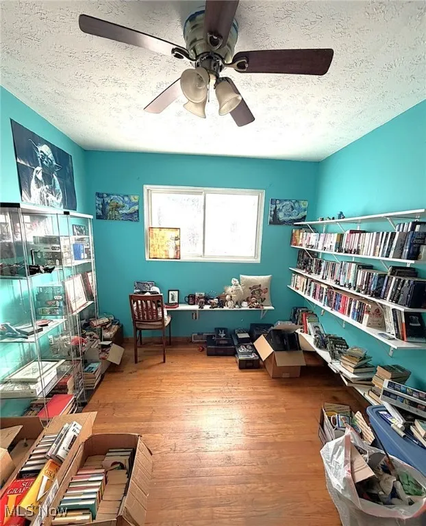 Living area with a textured ceiling, light wood-style flooring, and ceiling fan