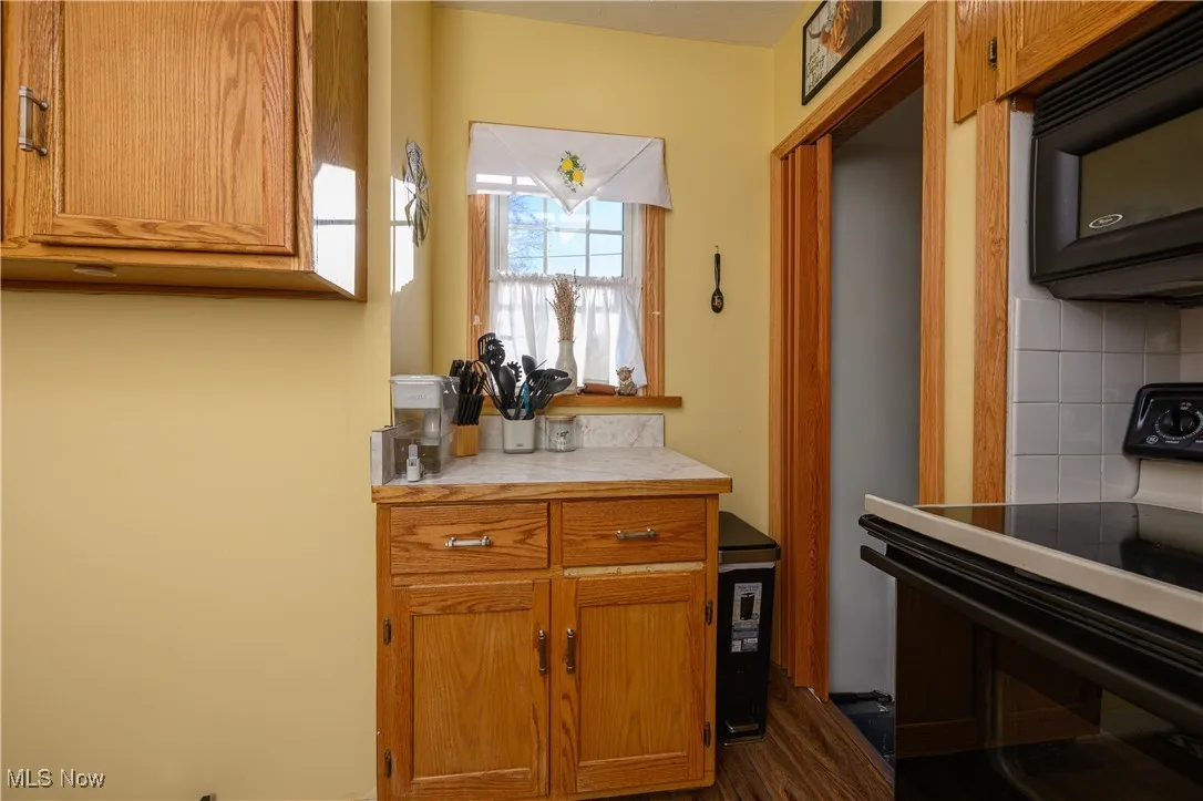 Kitchen featuring black appliances, brown cabinets, dark wood finished floors, and tile countertops