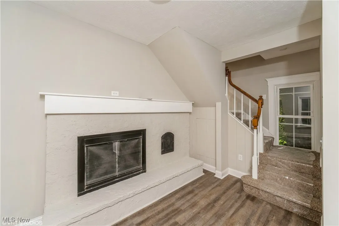 Unfurnished living room with a glass covered fireplace, stairs, wood finished floors, a textured ceiling, and vaulted ceiling