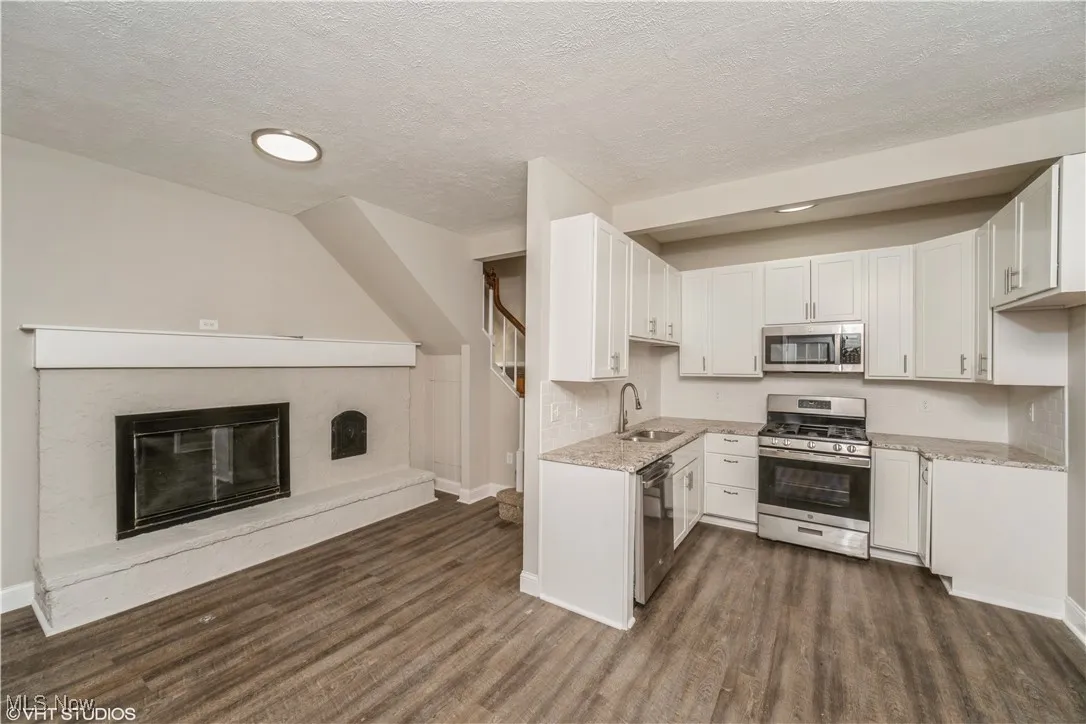 Kitchen with stainless steel appliances, a textured ceiling, open floor plan, a glass covered fireplace, and dark wood finished floors