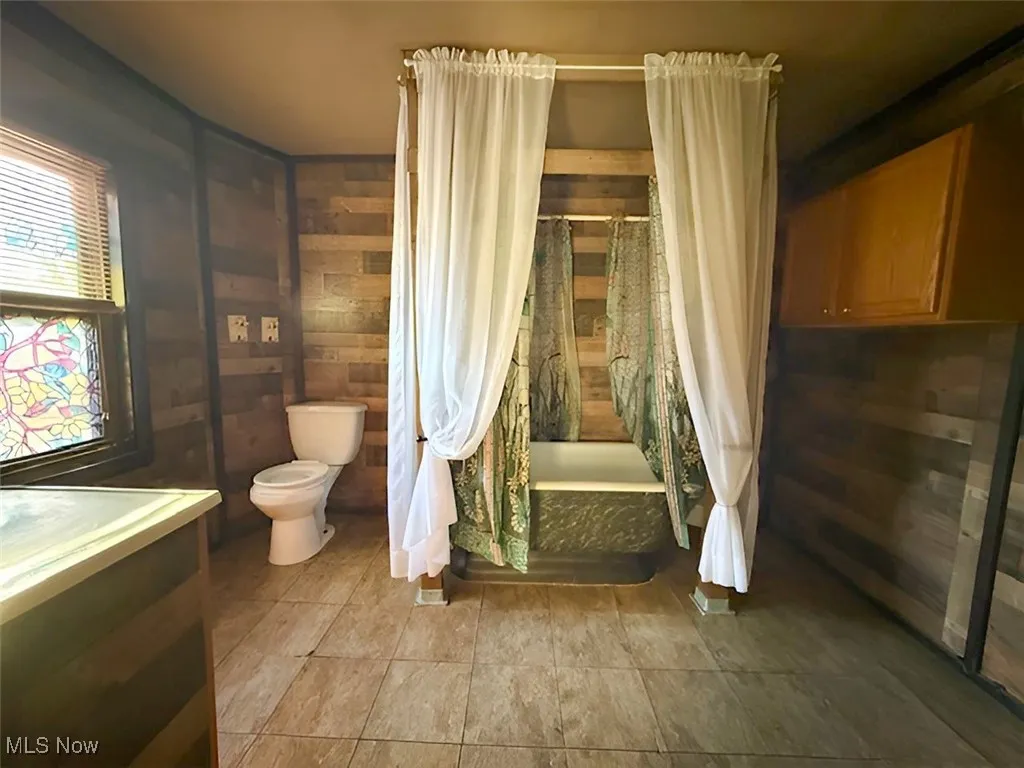 Full bath featuring wood walls, shower / bath combination with curtain, vanity, and tile patterned floors
