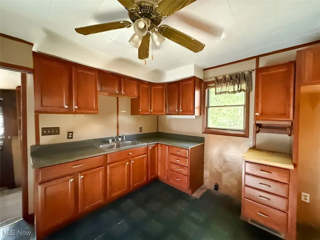 Kitchen featuring ceiling fan, brown cabinets, dark floors, and light countertops