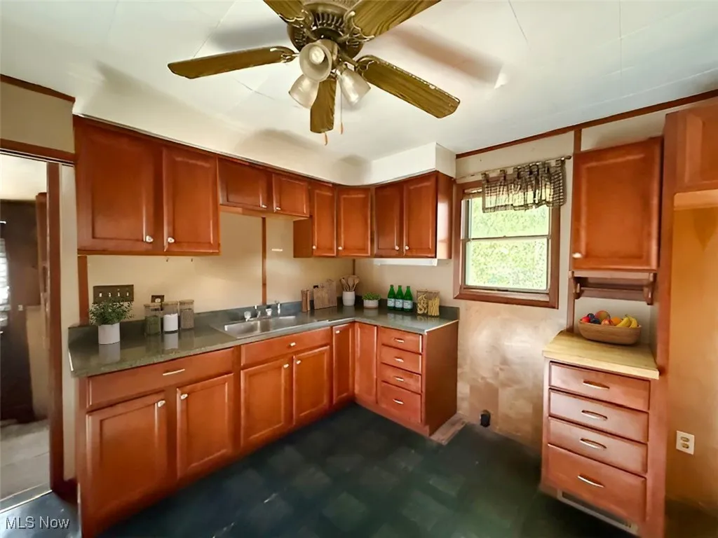 Kitchen with a ceiling fan, brown cabinets, light countertops, and dark floors