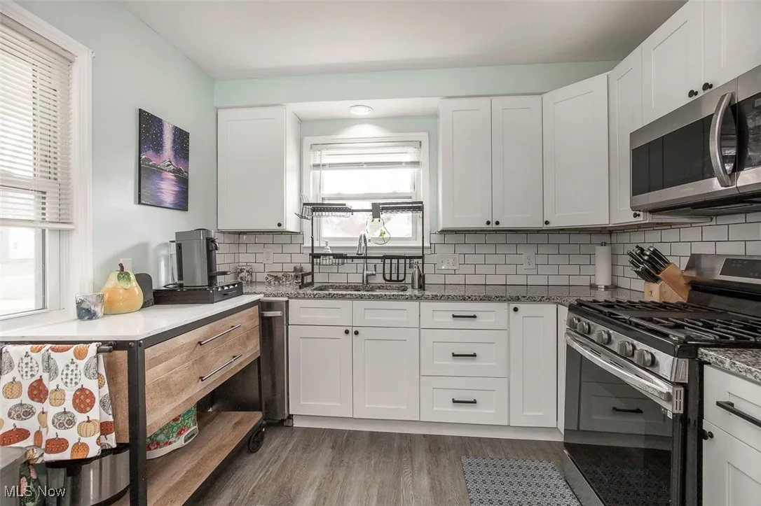 Kitchen with appliances with stainless steel finishes, white cabinets, light wood-type flooring, and dark stone counters