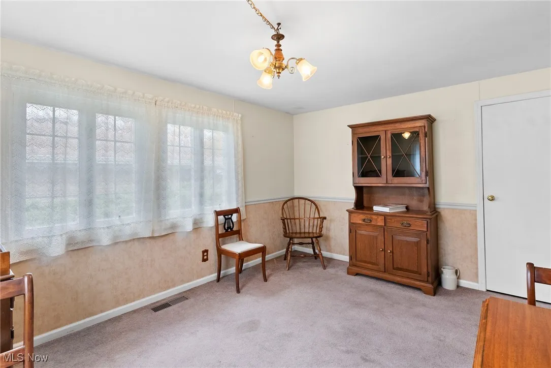 Living area with a chandelier, light colored carpet, and a wainscoted wall