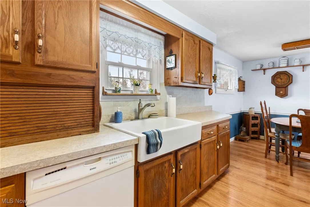Kitchen with brown cabinets, decorative backsplash, white dishwasher, light countertops, and light wood-style flooring