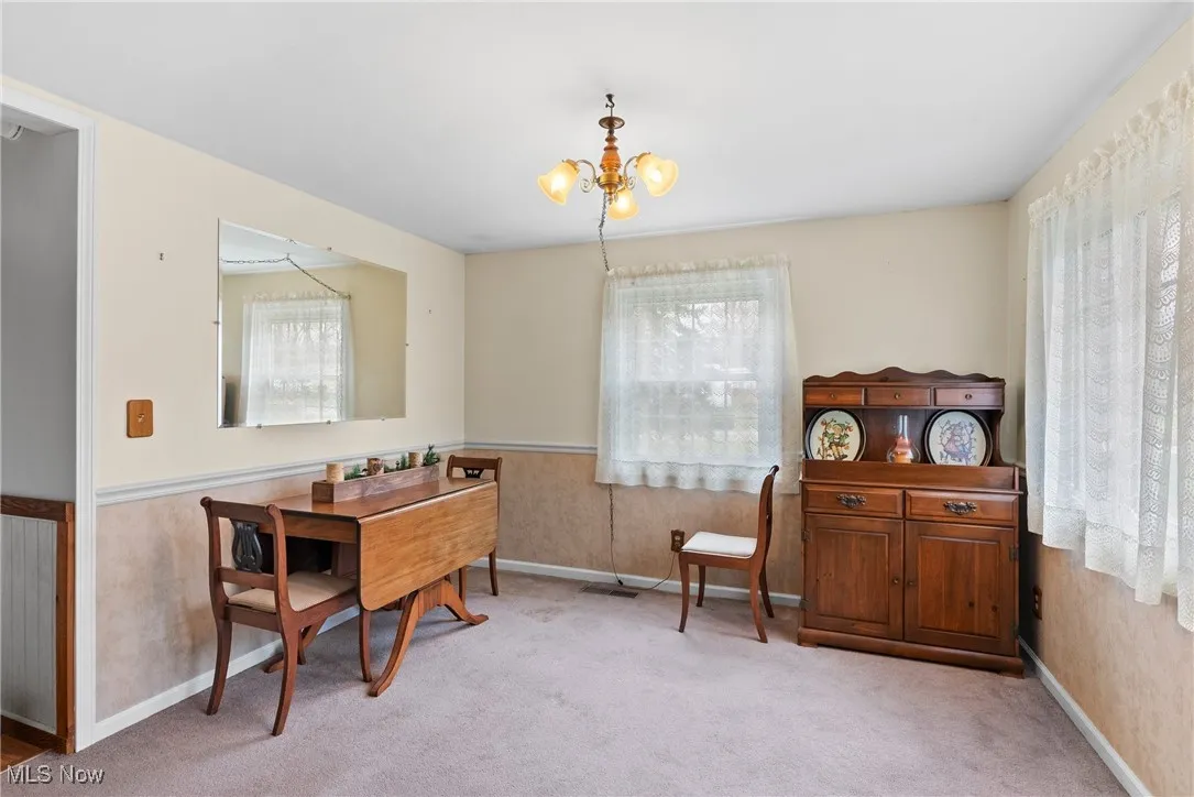 Living area featuring plenty of natural light, a chandelier, light carpet, and a wainscoted wall
