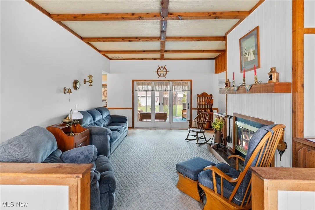 Carpeted living room with beamed ceiling, wood walls, a glass covered fireplace, and a wainscoted wall