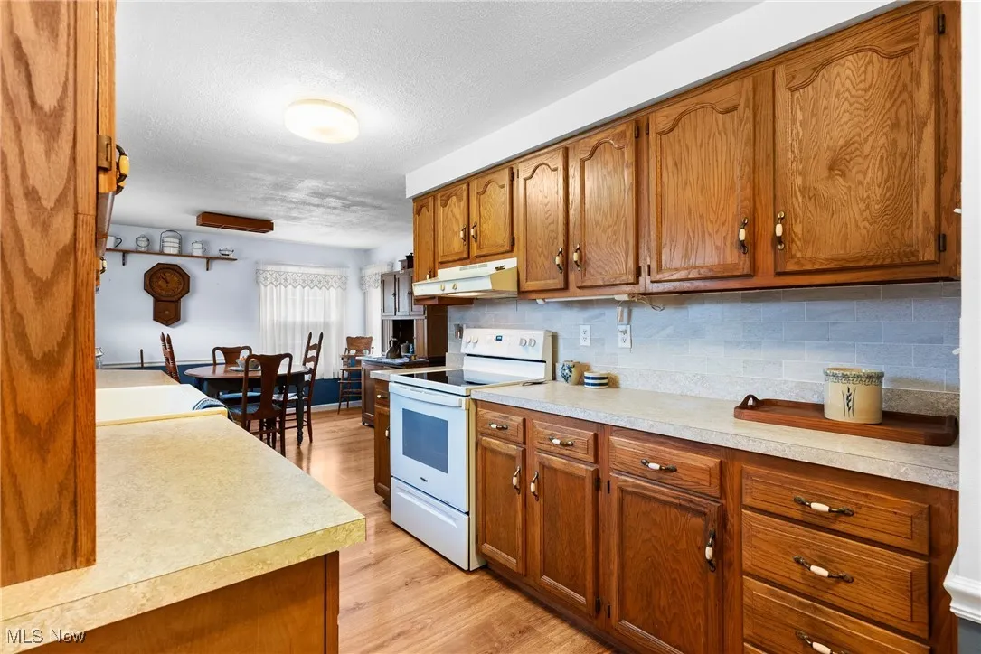 Kitchen featuring brown cabinetry, white electric range oven, tasteful backsplash, and a textured ceiling