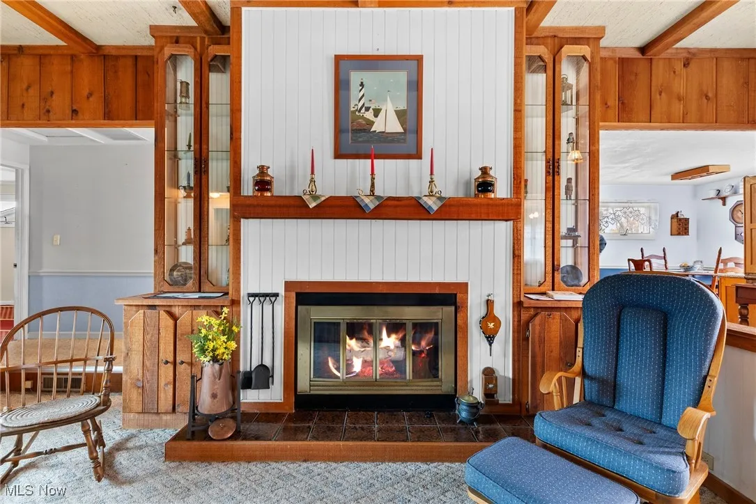 Living area with beam ceiling, wooden walls, and a glass covered fireplace