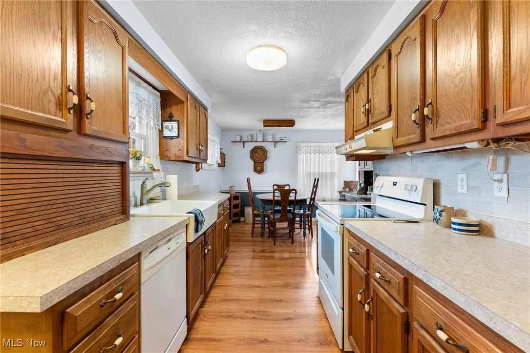 Kitchen with white appliances, brown cabinets, a textured ceiling, and light wood-style floors