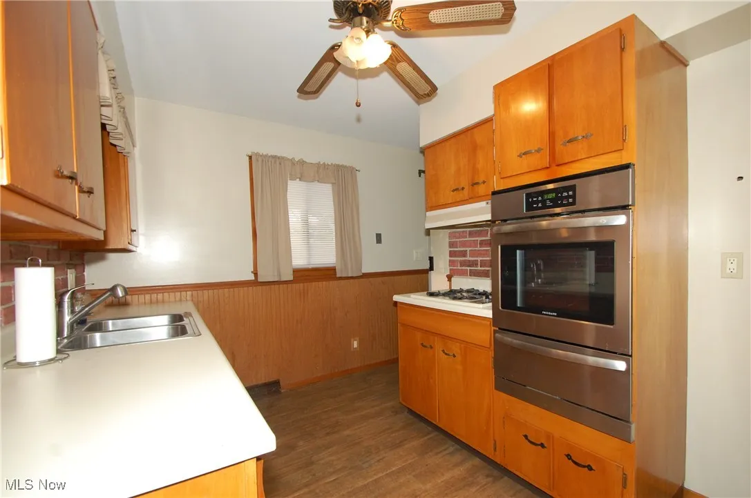 Kitchen with a wainscoted wall, appliances with stainless steel finishes, light countertops, a warming drawer, and wood walls