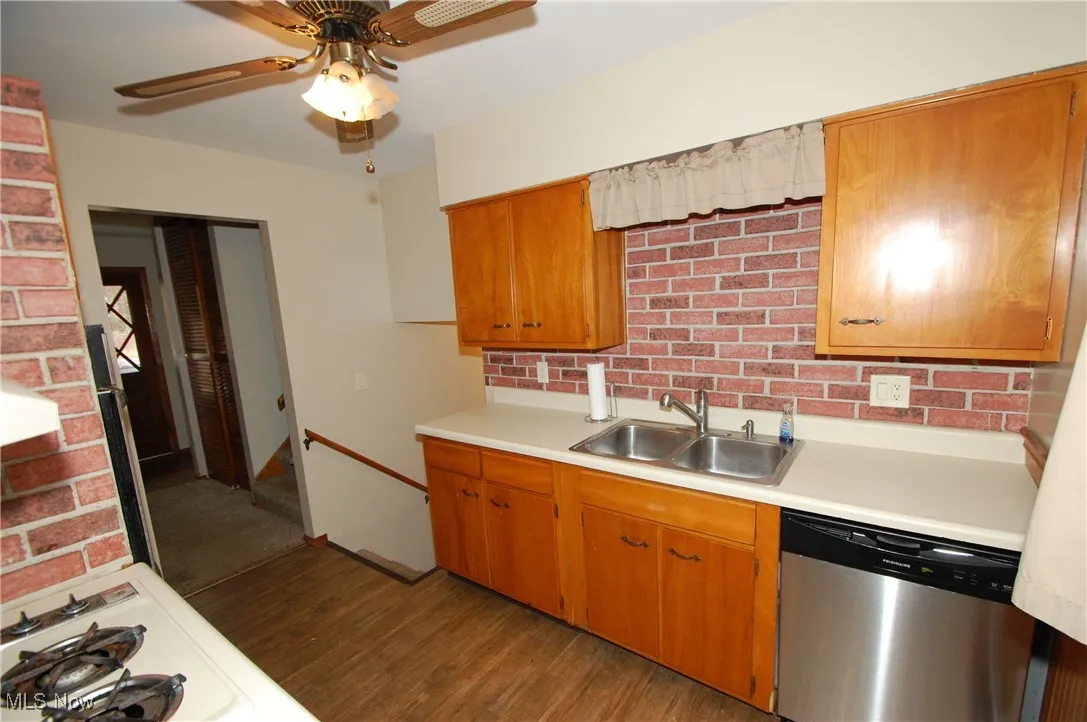 Kitchen featuring stainless steel dishwasher, light countertops, white gas cooktop, brown cabinets, and brick wall
