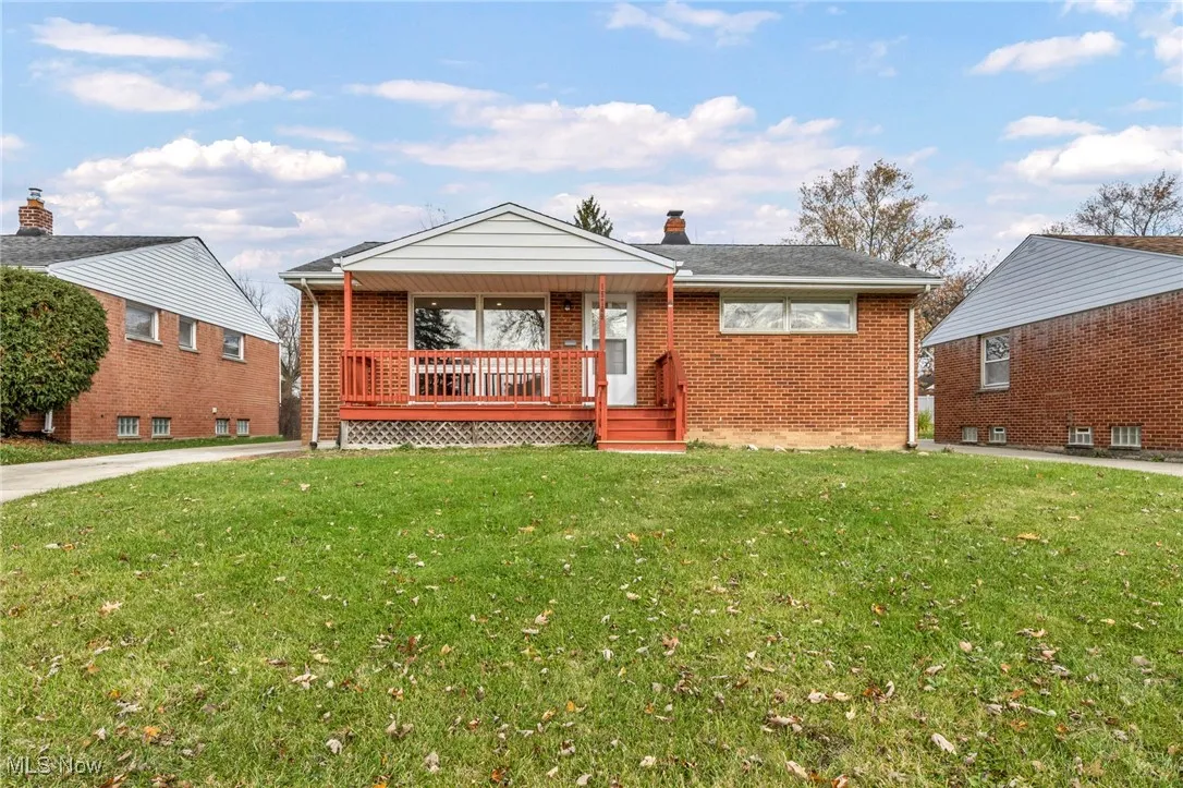 View of front of house with a front yard, brick siding, a chimney, and a porch