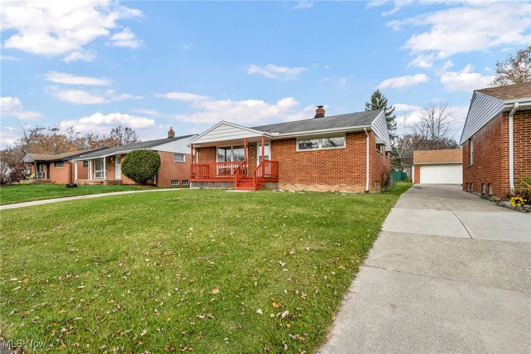 Ranch-style home with an outbuilding, brick siding, a front yard, a chimney, and a detached garage