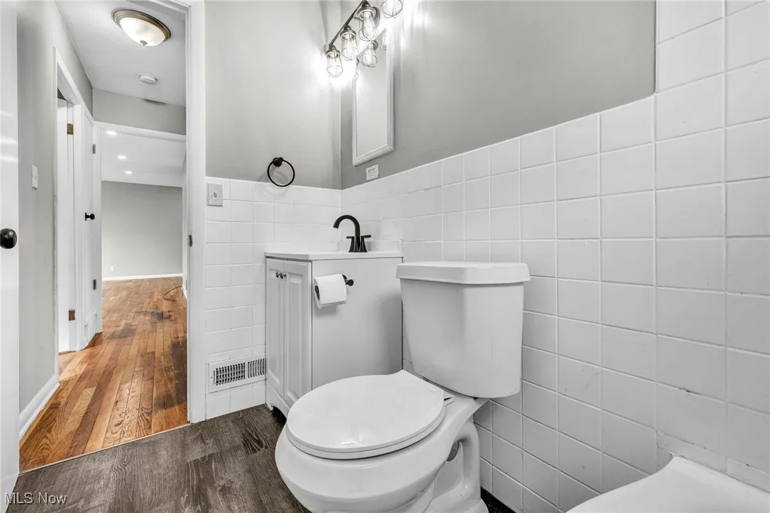 Half bathroom with tile walls, dark wood-style floors, vanity, and a wainscoted wall