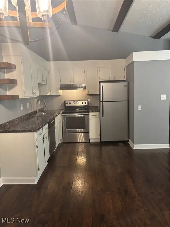 Kitchen with appliances with stainless steel finishes, dark wood-style flooring, dark stone countertops, range hood, and a textured ceiling