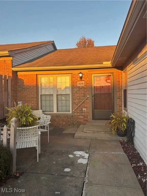 Doorway to property featuring brick siding and a shingled roof