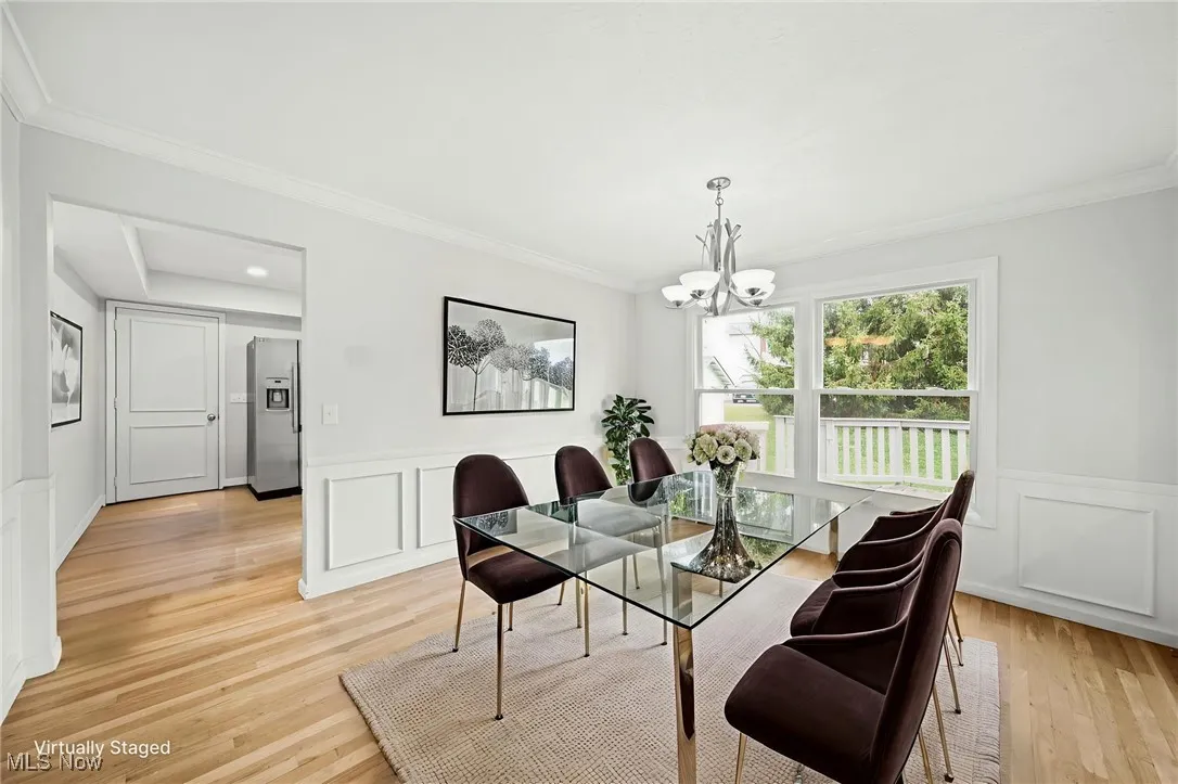 Dining space with a decorative wall, crown molding, light wood-type flooring, wainscoting, and a chandelier