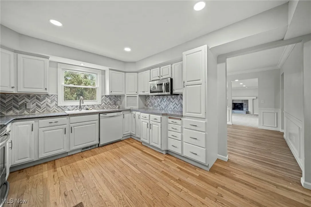 Kitchen featuring white cabinets, light wood-style flooring, appliances with stainless steel finishes, a fireplace, and recessed lighting