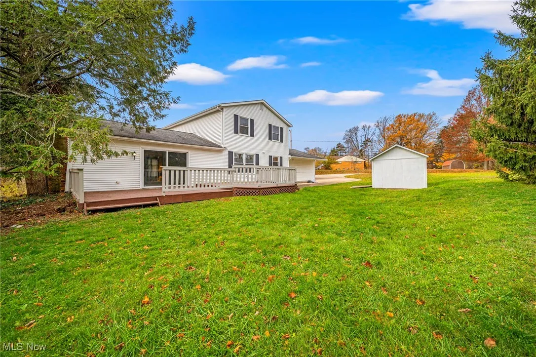 Rear view of house featuring a lawn, a wooden deck, and an outdoor structure