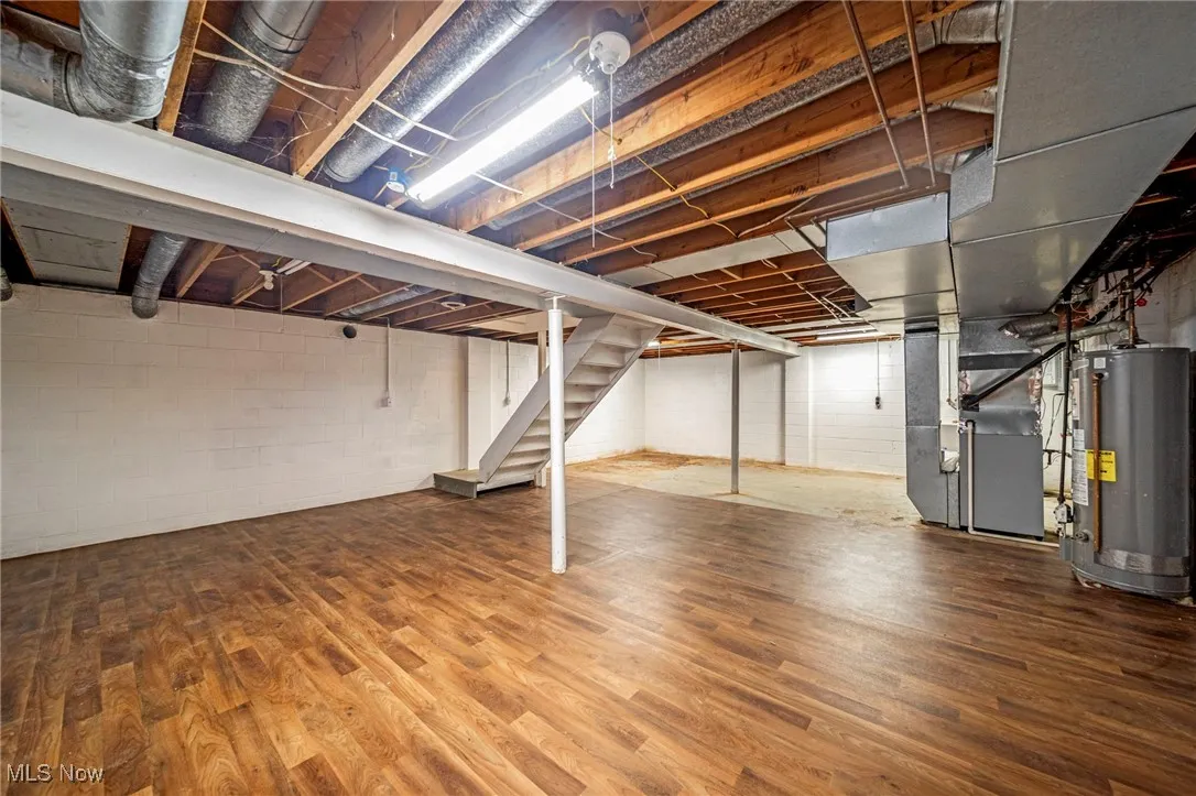 Unfinished basement with stairway, gas water heater, heating unit, and wood finished floors