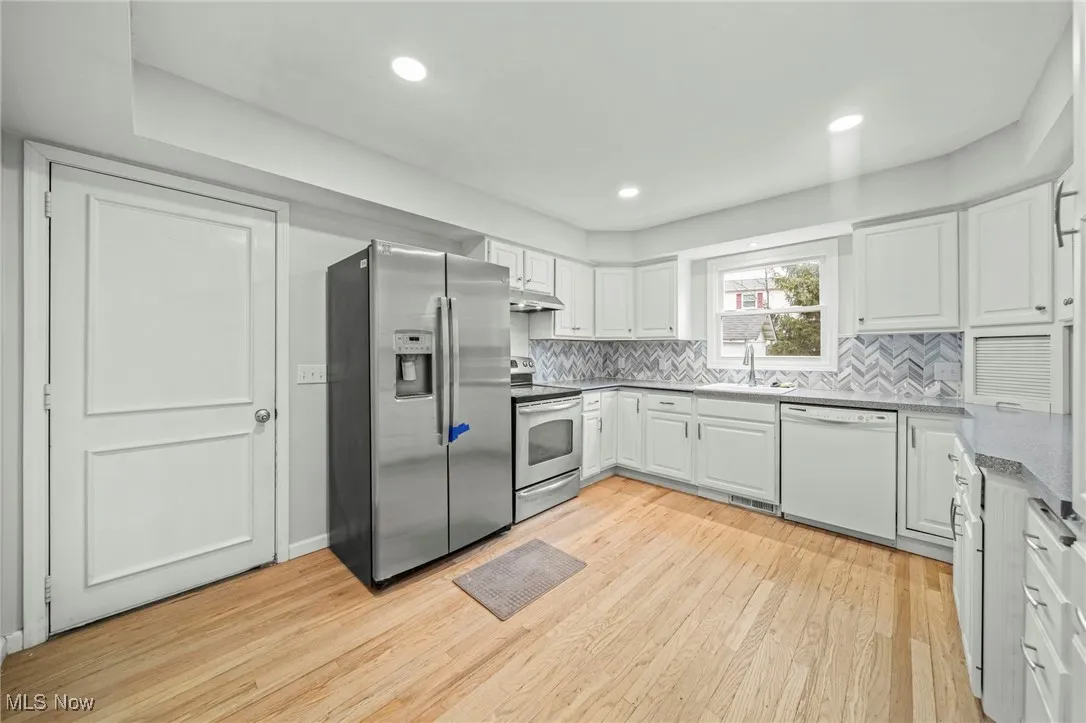 Kitchen featuring appliances with stainless steel finishes, white cabinets, backsplash, light wood finished floors, and dark stone countertops