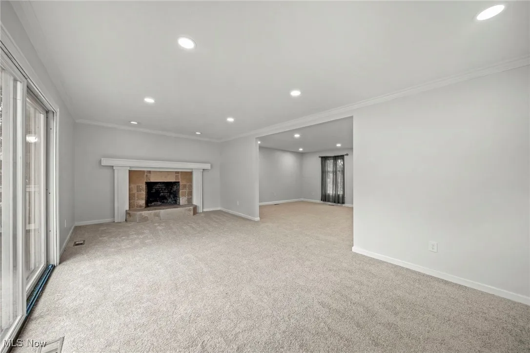 Unfurnished living room featuring ornamental molding, recessed lighting, carpet, a fireplace with raised hearth, and plenty of natural light
