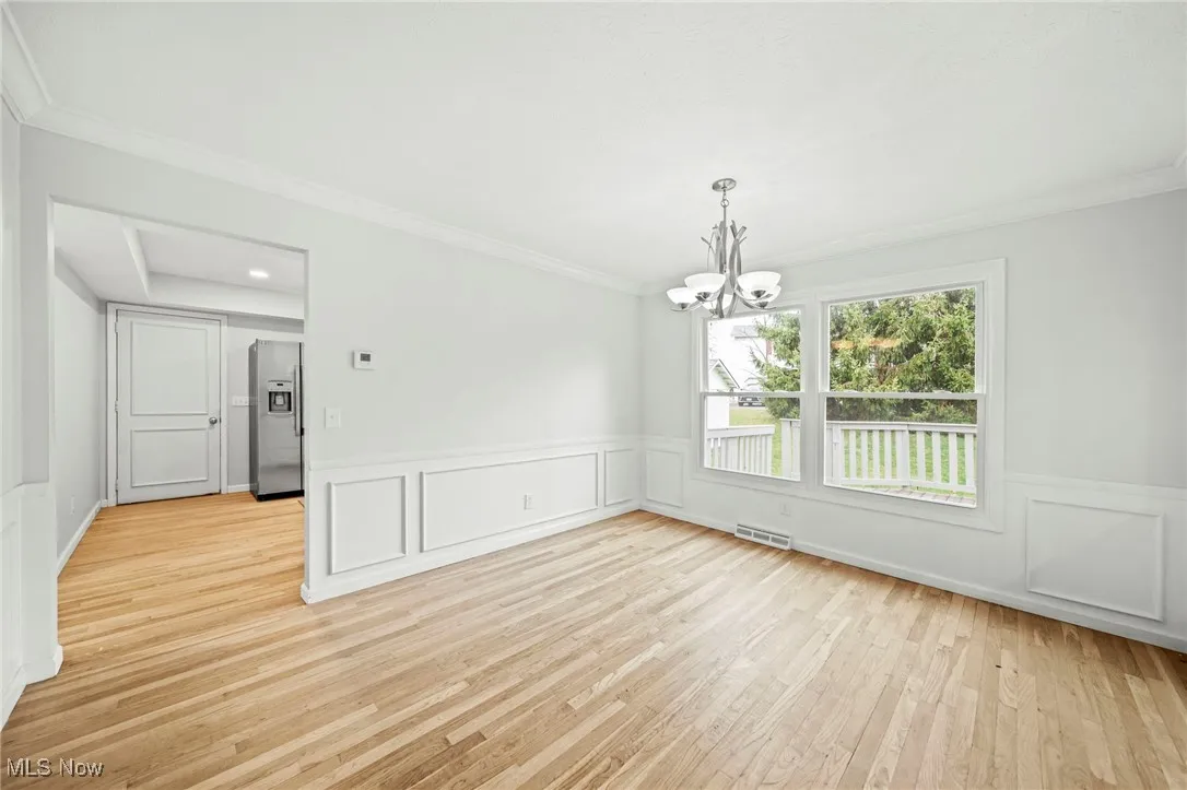 Spare room with ornamental molding, light wood-style flooring, a chandelier, a decorative wall, and wainscoting