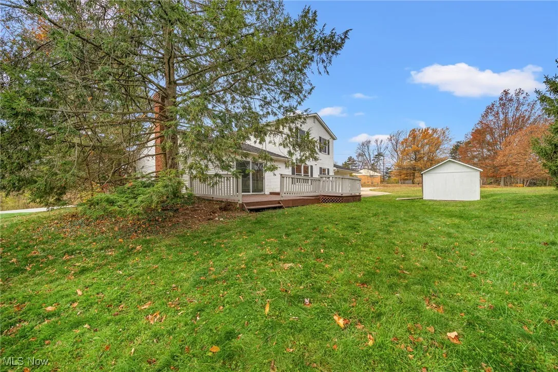 View of grassy yard with a wooden deck and a storage shed