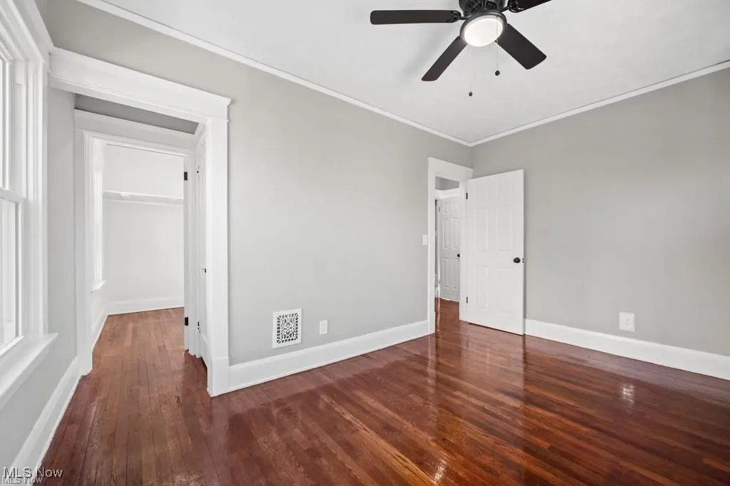 Unfurnished bedroom featuring dark wood-style flooring, ornamental molding, and ceiling fan