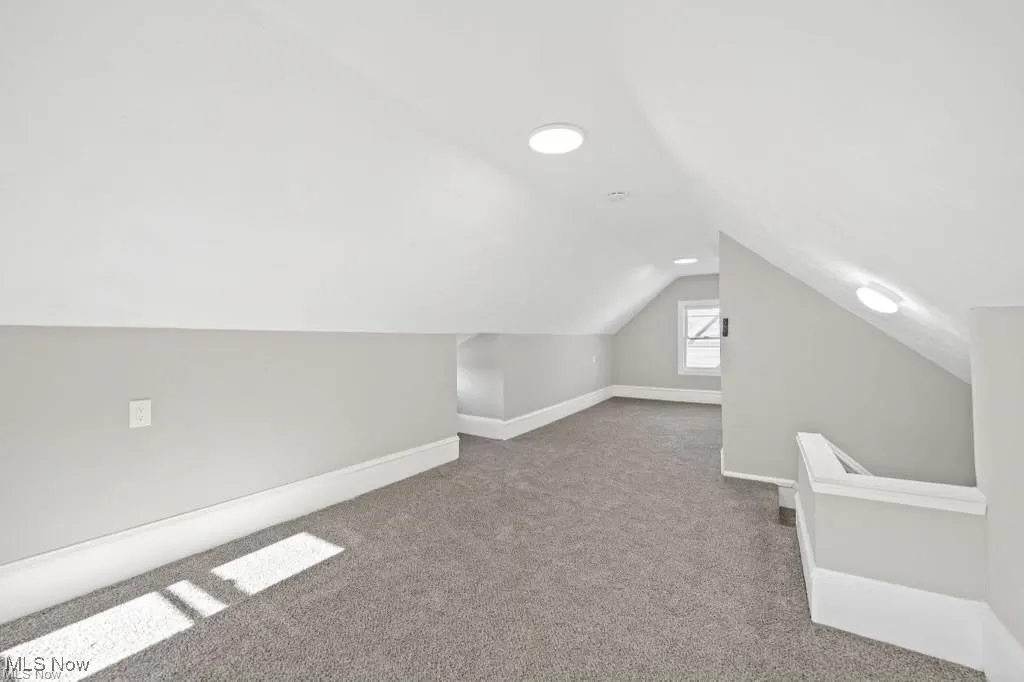 Bonus room with light colored carpet and vaulted ceiling
