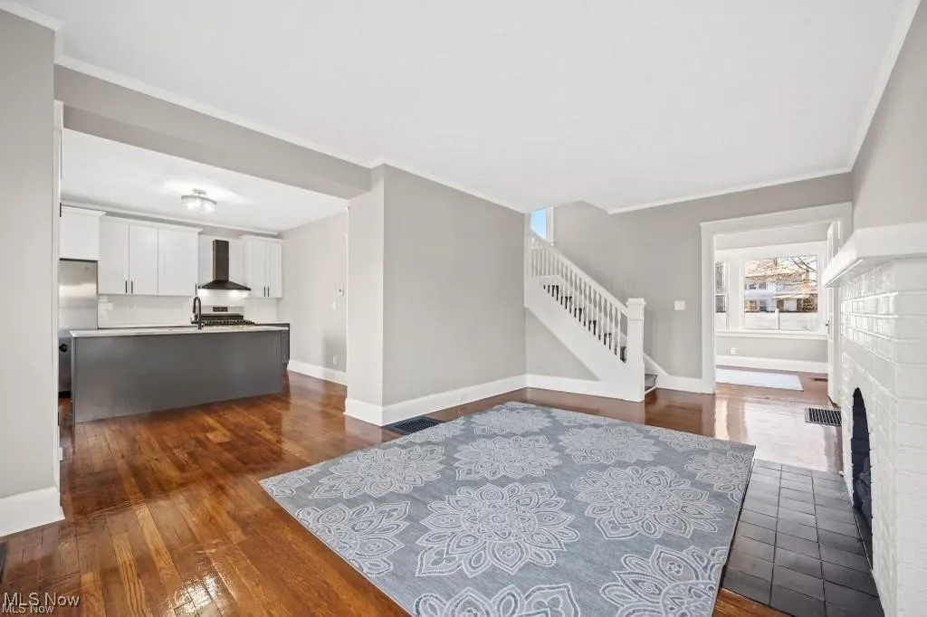 Living room featuring dark wood-type flooring, crown molding, stairway, and a fireplace