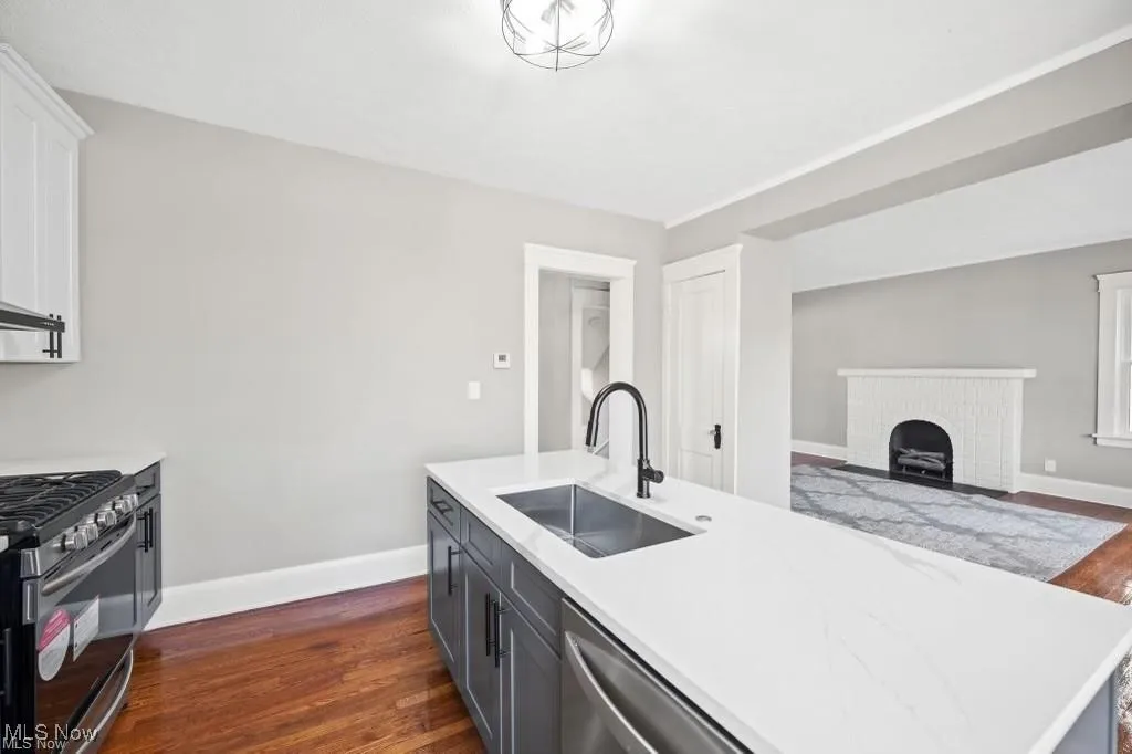 Kitchen featuring dark wood-type flooring, stainless steel appliances, white cabinetry, and light stone countertops