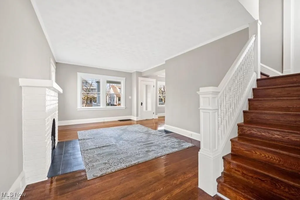 Foyer featuring stairs, dark wood finished floors, crown molding, and a fireplace