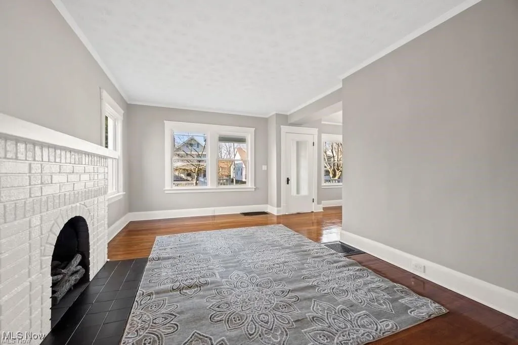 Living area with ornamental molding, a brick fireplace, and dark wood-style floors