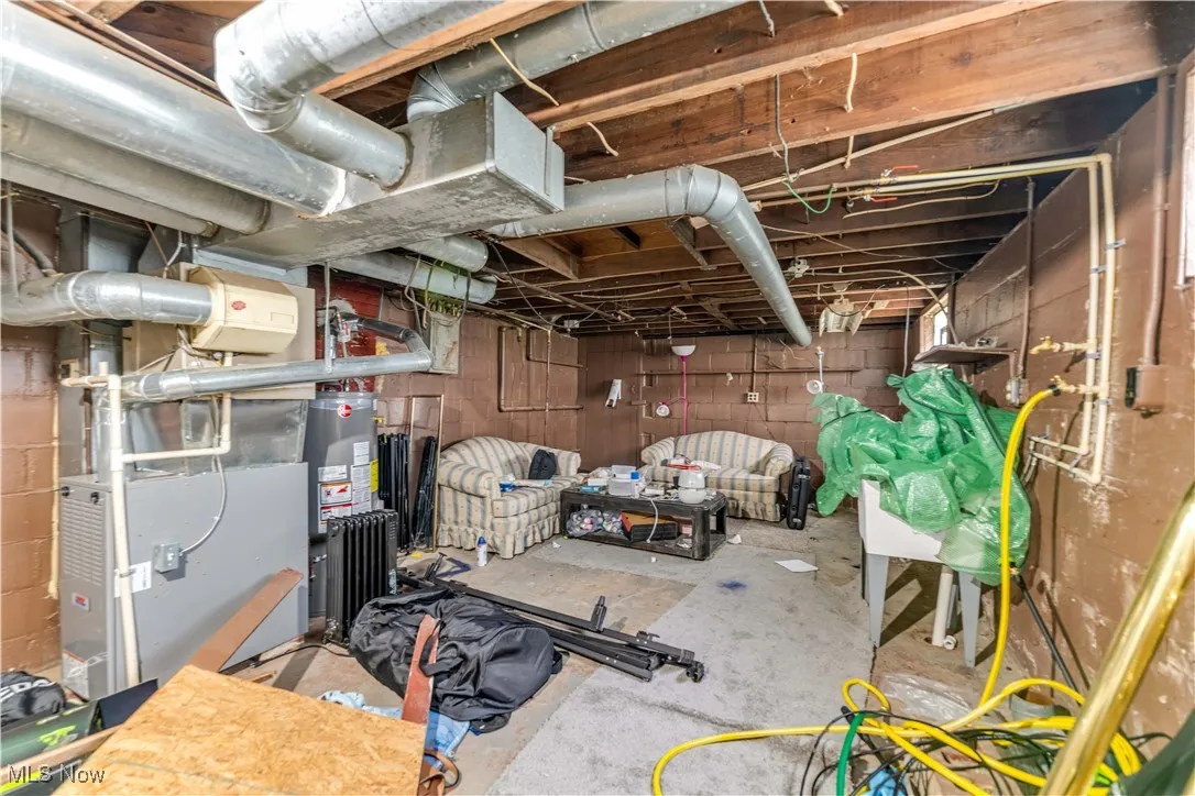 Unfinished basement with water heater, heating unit, and radiator