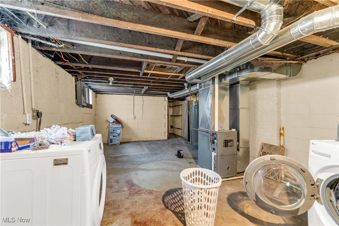 Unfinished below grade area featuring heating unit, water heater, washing machine and clothes dryer, and electric panel