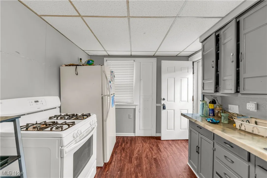 Kitchen with gray cabinets, gas range gas stove, a drop ceiling, dark wood-style floors, and light countertops
