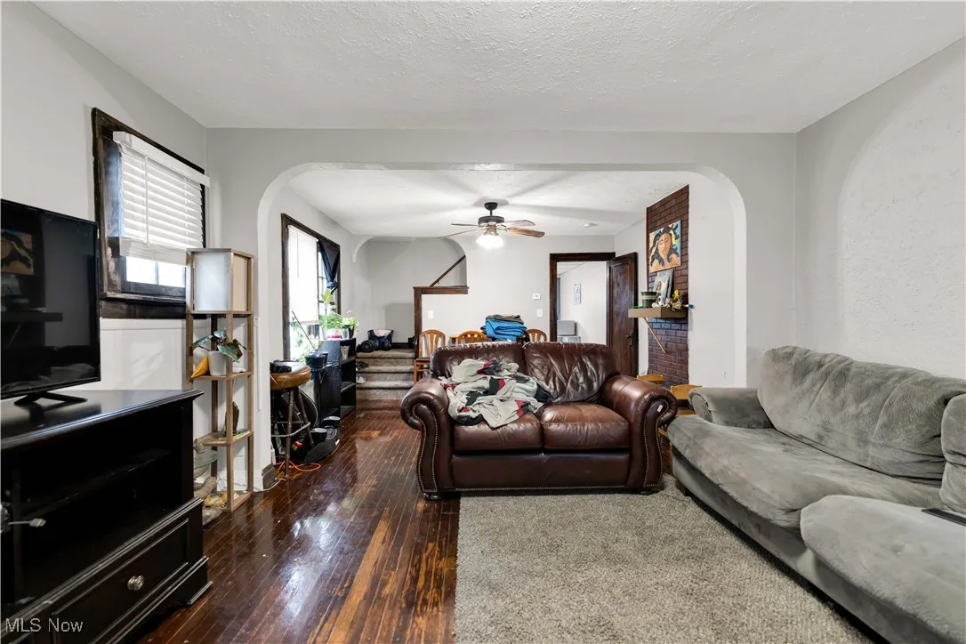 Living room featuring arched walkways, dark wood-style floors, a textured ceiling, and ceiling fan