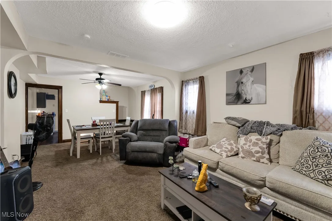 Carpeted living room with arched walkways, a textured ceiling, and a ceiling fan