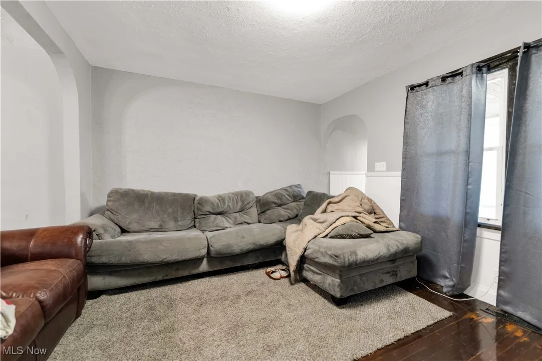Living room with arched walkways, dark wood finished floors, and a textured ceiling