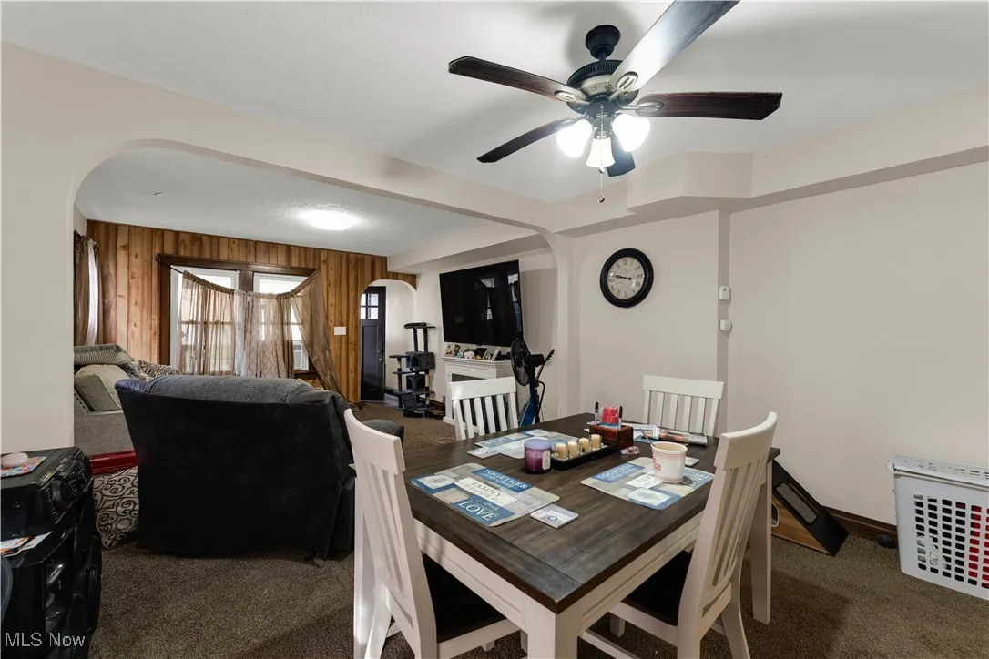 Dining area featuring dark colored carpet, arched walkways, wooden walls, and a ceiling fan