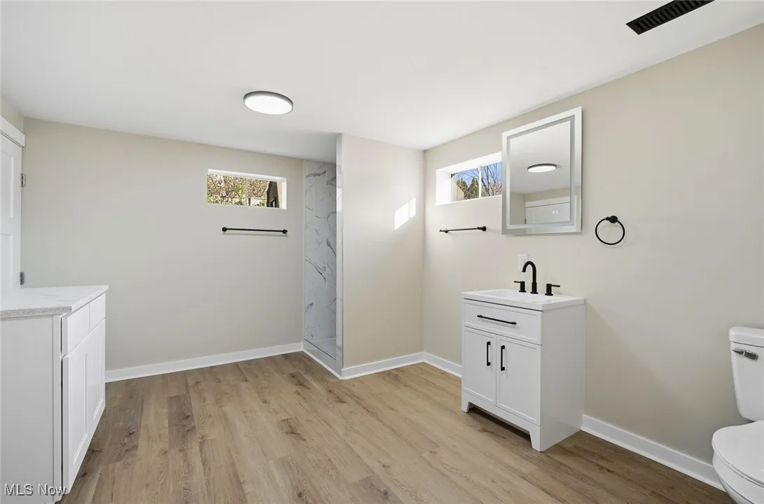 Full bath with light wood-style floors, vanity, and a marble finish shower