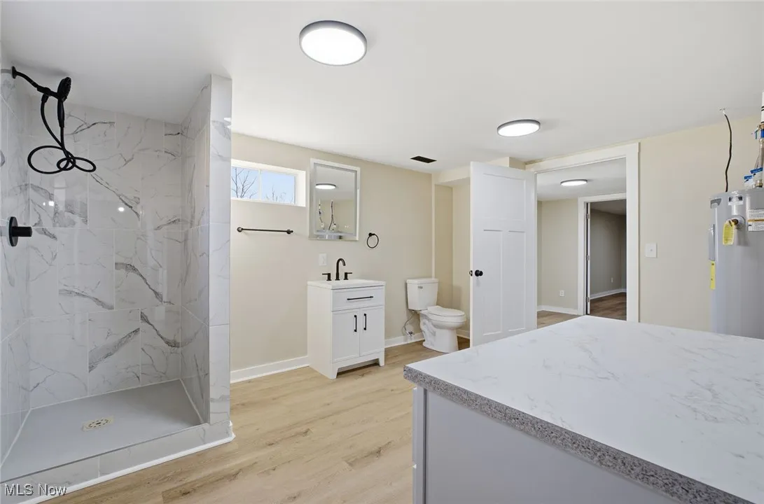 Bathroom featuring vanity, a marble finish shower, light wood finished floors, and water heater