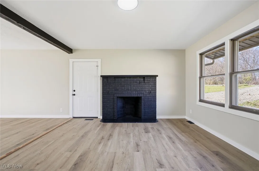 Unfurnished living room with a fireplace, light wood-type flooring, and beam ceiling